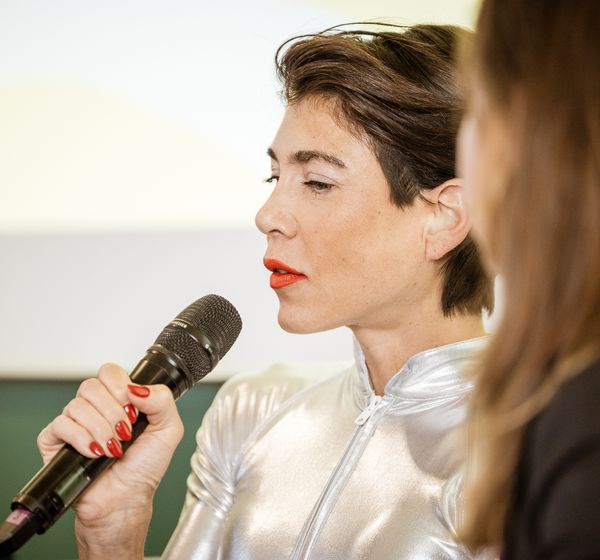 Speakerin im silbernen Outfit spricht ins Mikrofon